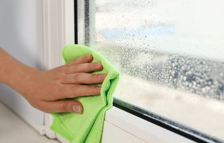 Een hand die met een doekje condens weghaalt aan de binnenkant van een raam.