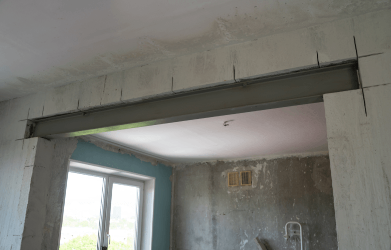 Een grote stalen H-balk boven de deuropening in een grijze muur van een renovatieproject.